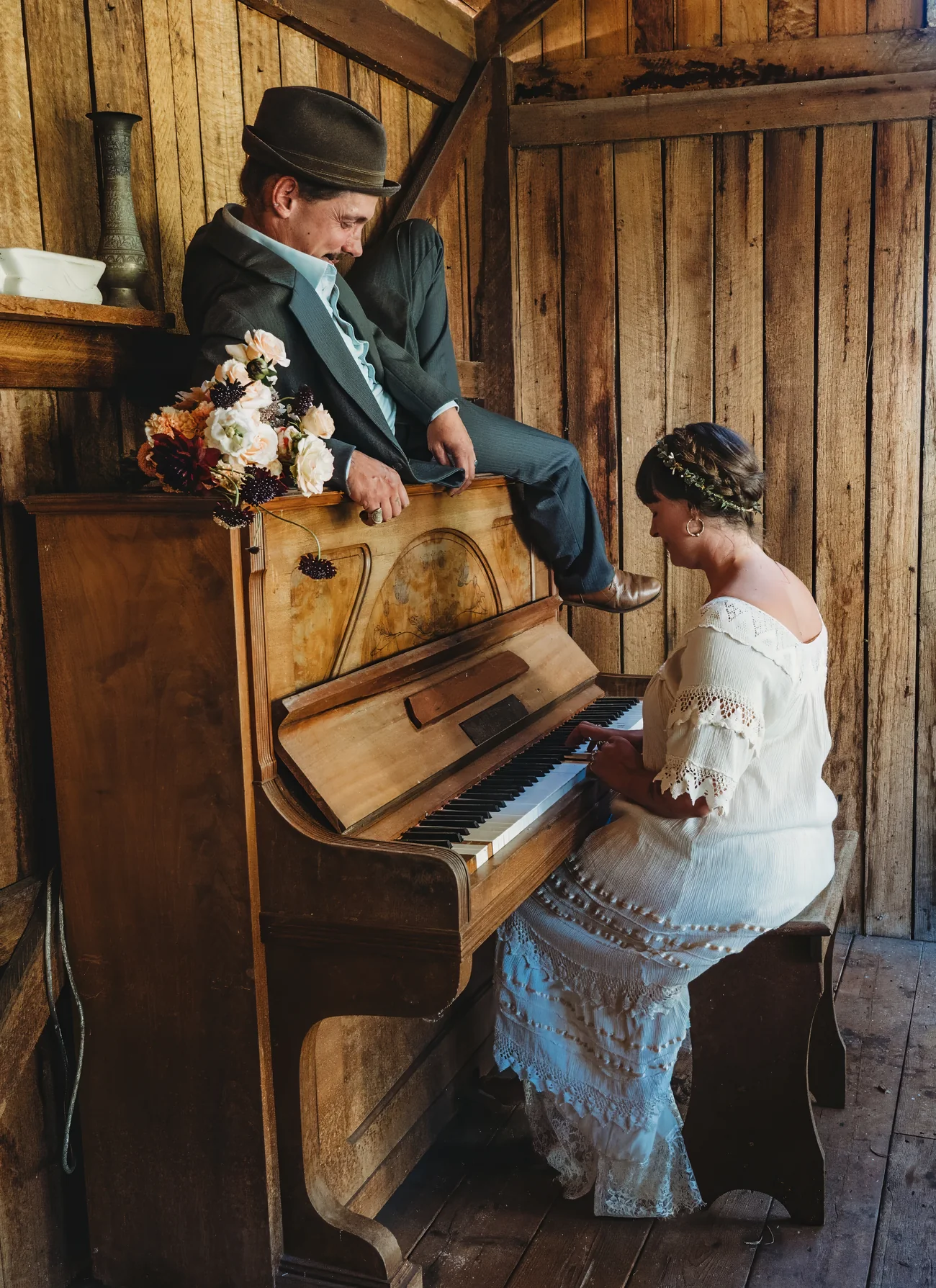 A newly married couple sharing a playful moment beside the piano in the Barn
