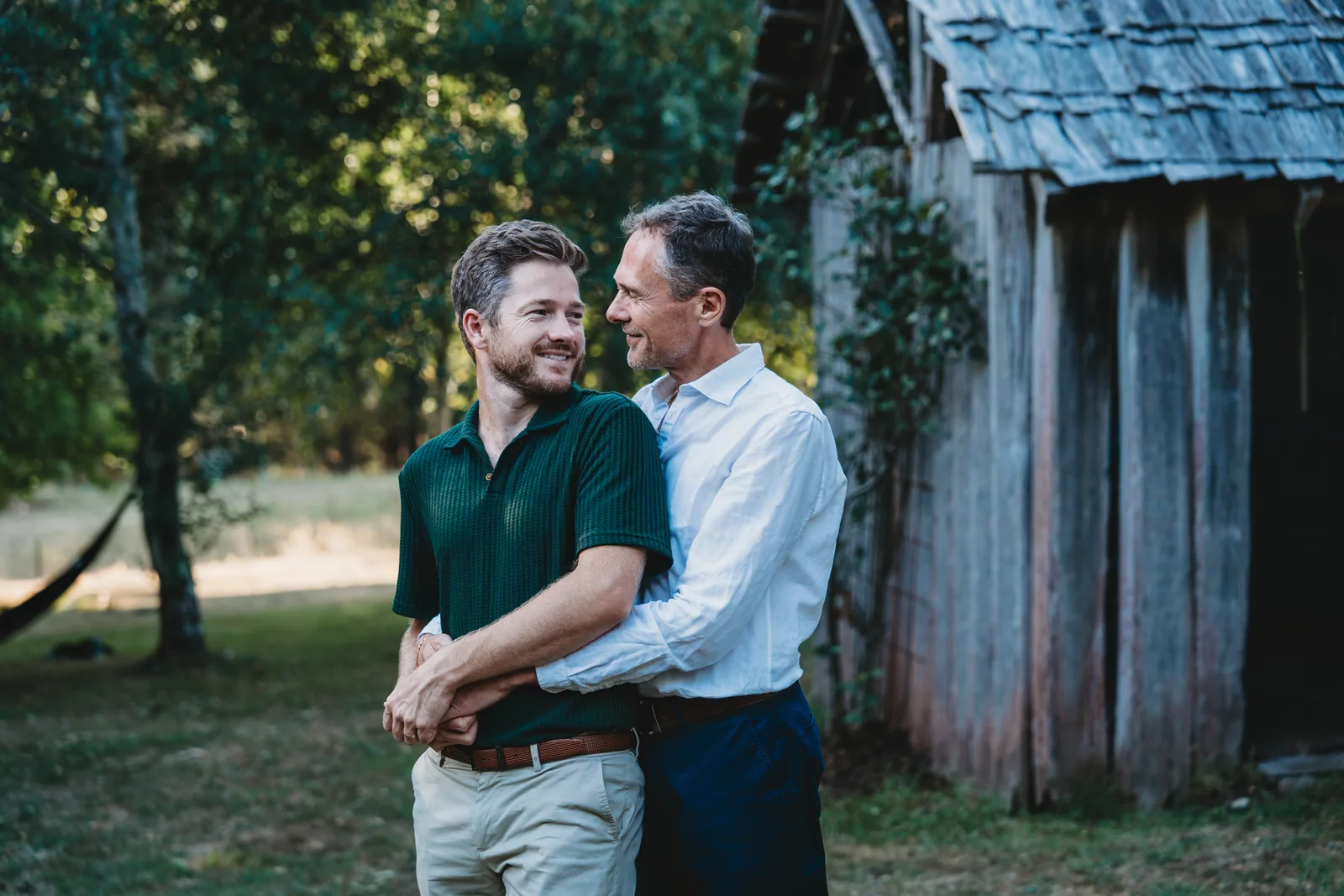 A couple embracing beside a rustic timber building at Whispering Woods