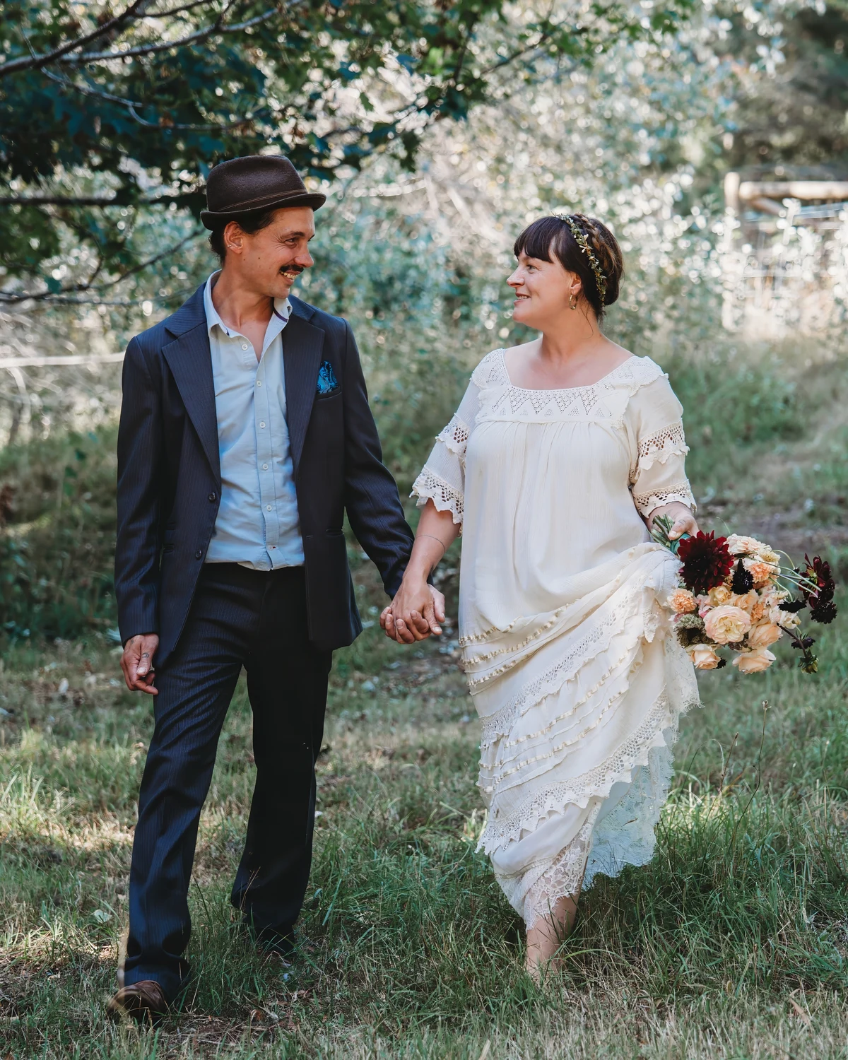 A newly married couple walking hand in hand through the woods at Whispering Woods